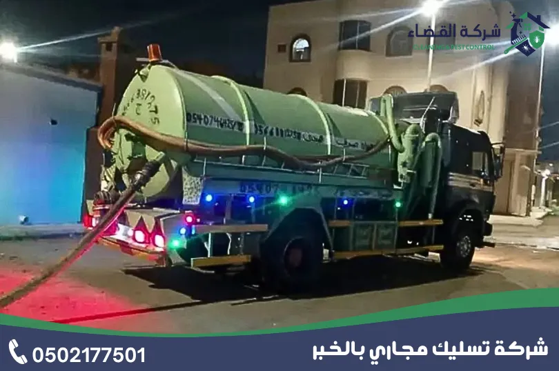 شفط بيارات بالخبر: سيارة شفط مجاري خضراء بخرطوم ممدود أمام مبنى في الليل
